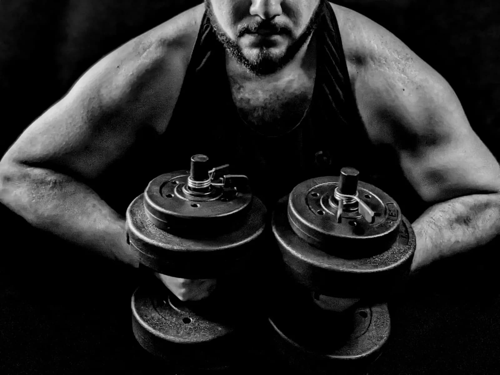 Black-and-white photo of Pedro holding two plate-loaded dumbbells at chest height