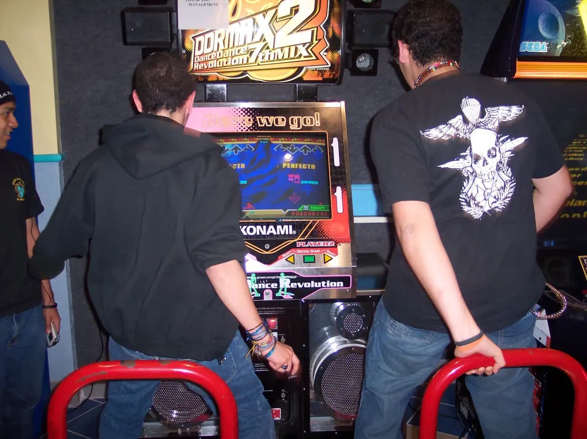 Two friends playing Dance Dance Revolution side by side at an arcade